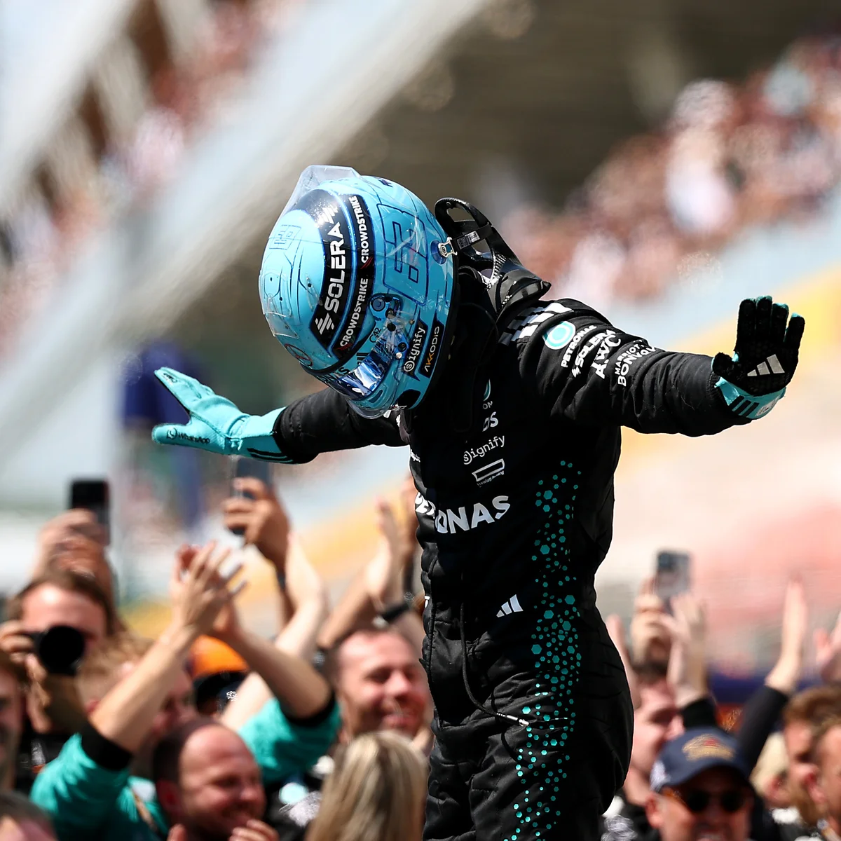 George Russell in his helmet, arms outstretched in the T-pose in front of the crowd